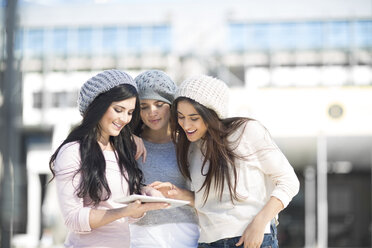 Three female friends with wool caps using digital tablet - ZEF000795