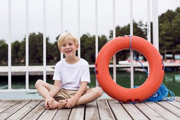 Portrait of smiling little boy sitting on a jetty besides a lifesaver - DAWF000110