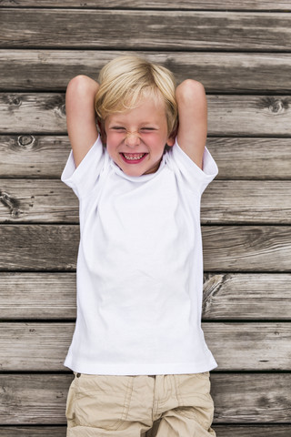 Porträt eines lachenden kleinen Jungen, der auf einem Steg liegt, lizenzfreies Stockfoto