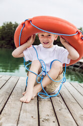 Porträt eines lächelnden kleinen Jungen, der auf einem Steg sitzt und mit einem Rettungsring spielt - DAWF000142