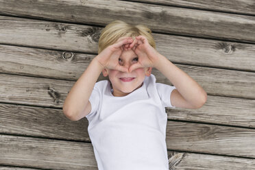 Portrait of little boy lying on a jetty shielding his eyes with his hands - DAWF000124