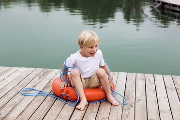 Portrait of smiling little boy sitting in a lifesaver on a jetty - DAWF000127