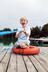 Porträt eines lachenden kleinen Jungen, der mit einem Rettungsring auf einem Steg spielt - DAWF000128