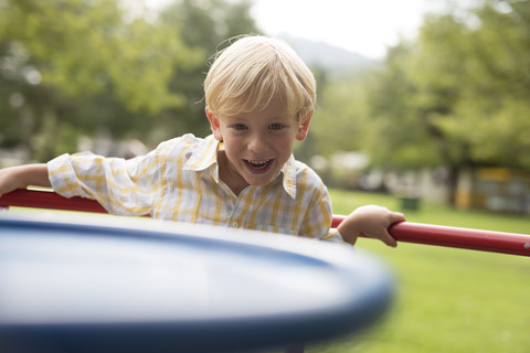 Porträt eines lächelnden kleinen Jungen, der auf einem Karussell auf einem Spielplatz steht, lizenzfreies Stockfoto