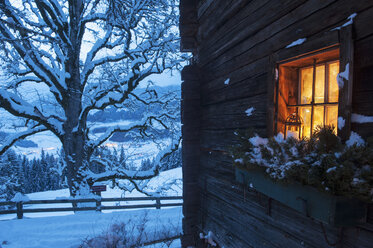 Österreich, Land Salzburg, Altenmarkt-Zauchensee, Fassade einer Holzhütte mit beleuchtetem Fenster im Winter - HHF004865