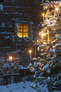 Österreich, Land Salzburg, Altenmarkt-Zauchensee, Fassade einer Holzhütte mit beleuchtetem Christbaum im Vordergrund - HHF004874