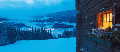 Österreich, Land Salzburg, Altenmarkt-Zauchensee, Fassade einer Holzhütte mit beleuchtetem Fenster im Winter, lizenzfreies Stockfoto