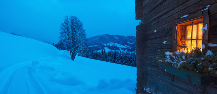 Österreich, Land Salzburg, Altenmarkt-Zauchensee, Fassade einer Holzhütte mit beleuchtetem Fenster im Winter - HHF004861