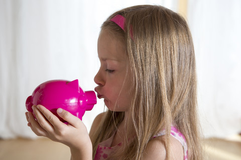 Little girl kissing her pink piggy bank stock photo