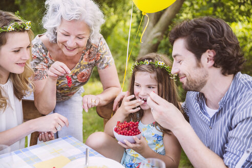 Familie genießt eine Schale mit roten Johannisbeeren am Tisch im Freien - MFF001265