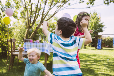 Children trying to catch soap bubbles in garden - MFF001275