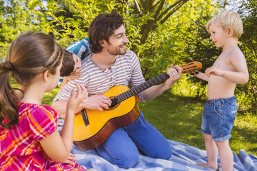 Vater mit Kindern spielt Gitarre im Garten - MFF001303
