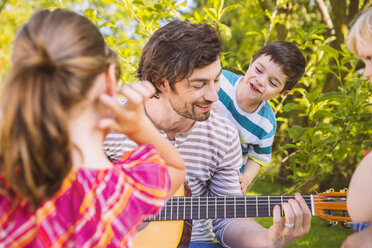 Vater mit Kindern spielt Gitarre im Garten - MFF001304
