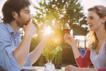 Couple clinking red wine glasses at table in evening light - MFF001327