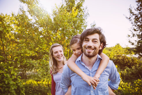 Glückliche dreiköpfige Familie im Garten bei Sonnenuntergang - MFF001322