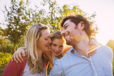 Glückliche dreiköpfige Familie im Garten bei Sonnenuntergang - MFF001323