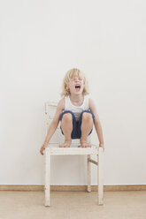 Portrait of screaming little boy crounching on a chair - MJF001331