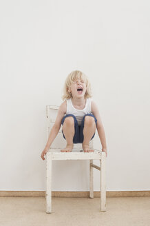 Portrait of screaming little boy crounching on a chair - MJF001331