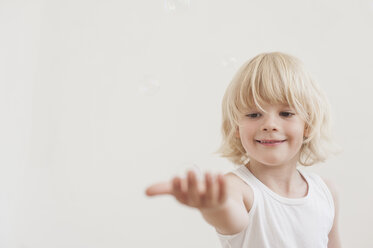 Portrait of smiling little boy with outstretched arm watching a soap bubble - MJF001336