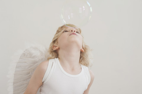 Portrait of little boy with angel wings blowing a soap bubble stock photo