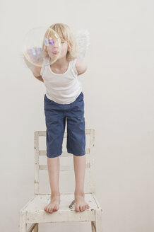 Porträt eines kleinen Jungen mit Winkelflügeln, der eine Seifenblase beobachtet - MJF001346