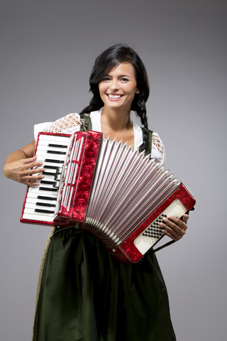 Porträt einer lächelnden jungen Frau mit Akkordeon und Dirndl, lizenzfreies Stockfoto