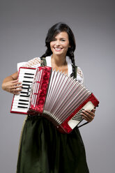 Portrait of smiling young woman with accordion wearing dirndl - MAEF009041