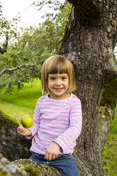 Porträt eines lächelnden kleinen Mädchens mit einem Apfel, das auf einem Apfelbaum sitzt - LVF001794