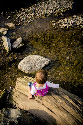 Little girl sitting on deadwood at riverside stock photo