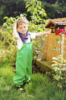 Portrait of little boy wearing green dungarees standing in the garden - AFF000084