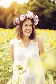 Porträt einer lächelnden jungen Frau mit Blumen, die in einem Sonnenblumenfeld steht - AFF000144