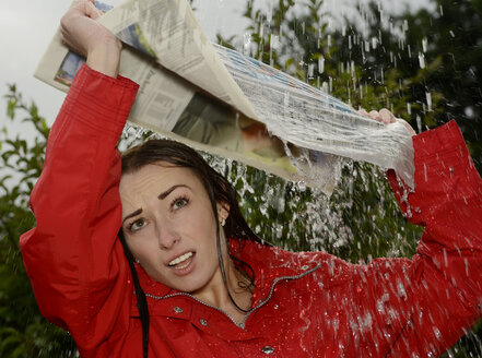 Porträt einer jungen Frau bei Regen, die eine Zeitung über ihren Kopf hält - BFRF000509