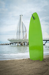 Mexiko, Jalisco, Puerto Vallarta, Surfbrett im Sand am Strand Los Muertos mit Pier im Hintergrund - ABAF001462