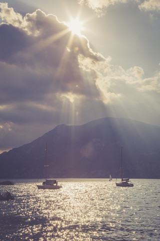 Italien, Venetien, Brenzone, Segelboote auf dem Gardasee im Gegenlicht der Sonne, lizenzfreies Stockfoto