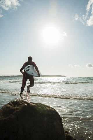 Frankreich, Bretagne, Camaret-sur-Mer, Jugendlicher mit Surfbrett am Meer, lizenzfreies Stockfoto