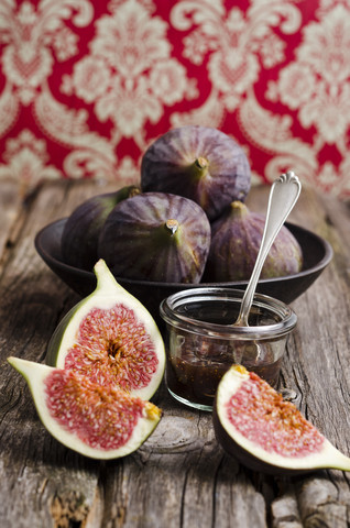 Geschnittene und ganze Feigen und ein Glas Feigenmarmelade auf einem Holztisch, lizenzfreies Stockfoto