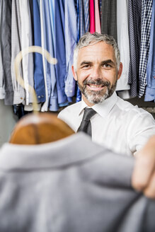 Porträt eines Geschäftsmannes, der eine Jacke in seinem begehbaren Kleiderschrank auswählt - MBEF001192