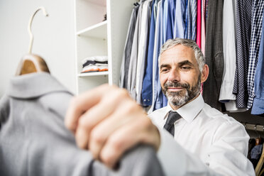 Portrait of businessman choosing jacket at his walk-in closet - MBEF001193