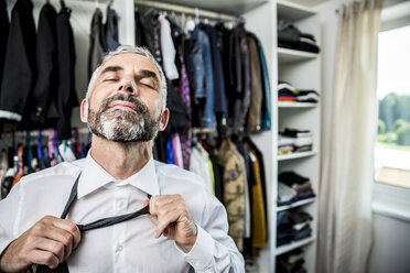 Businessman binding tie at his walk-in closet - MBEF001195