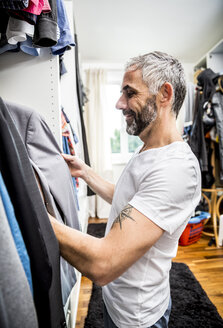 Mann wählt Kleidung in seinem begehbaren Kleiderschrank aus - MBEF001199
