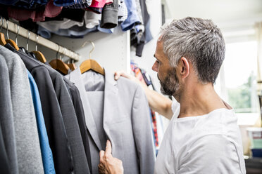 Mann wählt Kleidung in seinem begehbaren Kleiderschrank aus - MBEF001200