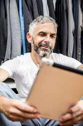 Man with his digital tablet sitting on the floor of his walk-in closet - MBEF001206