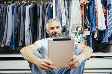 Man with his digital tablet sitting on the floor of his walk-in closet - MBEF001208