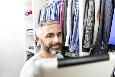 Mann mit seinem digitalen Tablet in seinem begehbaren Kleiderschrank - MBEF001210