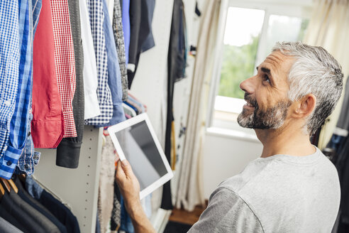 Mann mit seinem digitalen Tablet in seinem begehbaren Kleiderschrank - MBEF001211