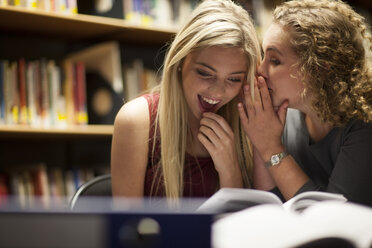 Zwei Studentinnen flüstern in einer Bibliothek - ZEF000828