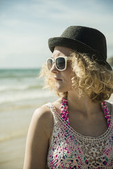 Porträt eines jungen Mädchens mit Hut und Sonnenbrille am Ufer des Strandes - UUF001676