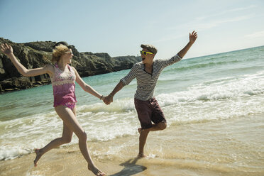 Teenagerpaar läuft Hand in Hand am Ufer des Strandes - UUF001677