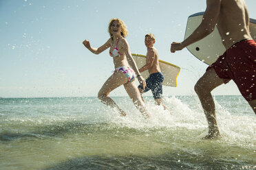 Three teenagers with surfboards running at waterside of the sea - UUF001685