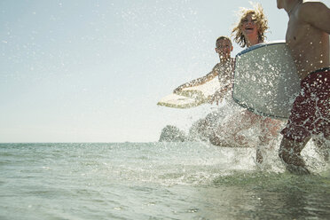 Three teenagers with surfboards running at waterside of the sea - UUF001687